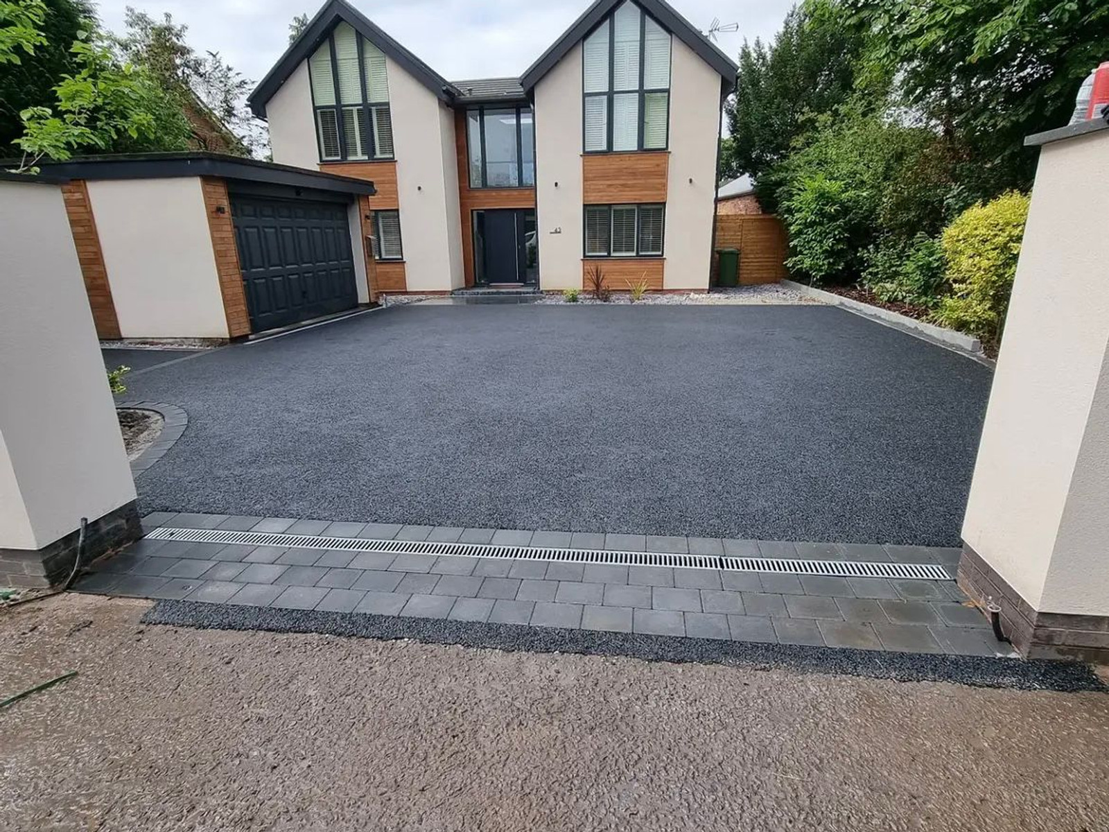 Finished dark charcoal driveway with patios drainage channel in front of a modern home