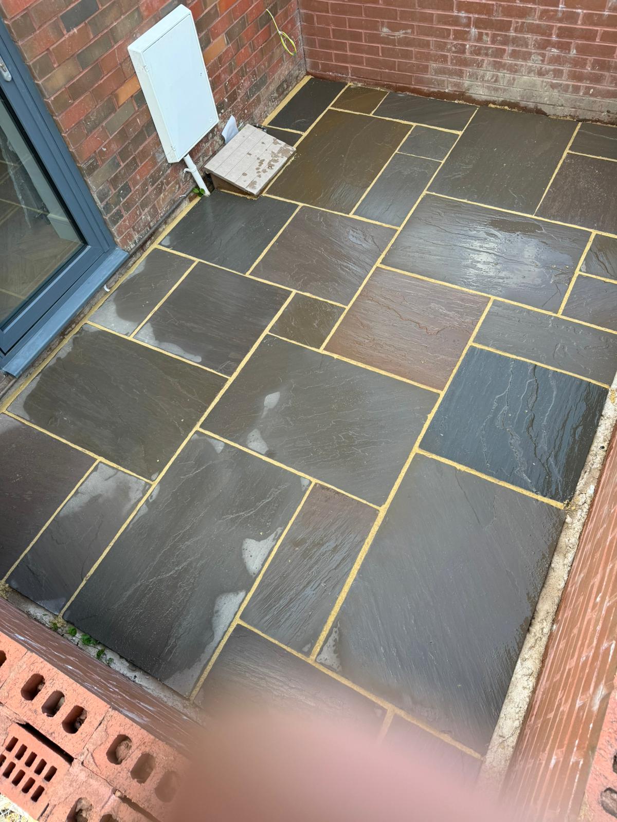 Patio stone paving in progress beside brick walls — Sale, Cheshire