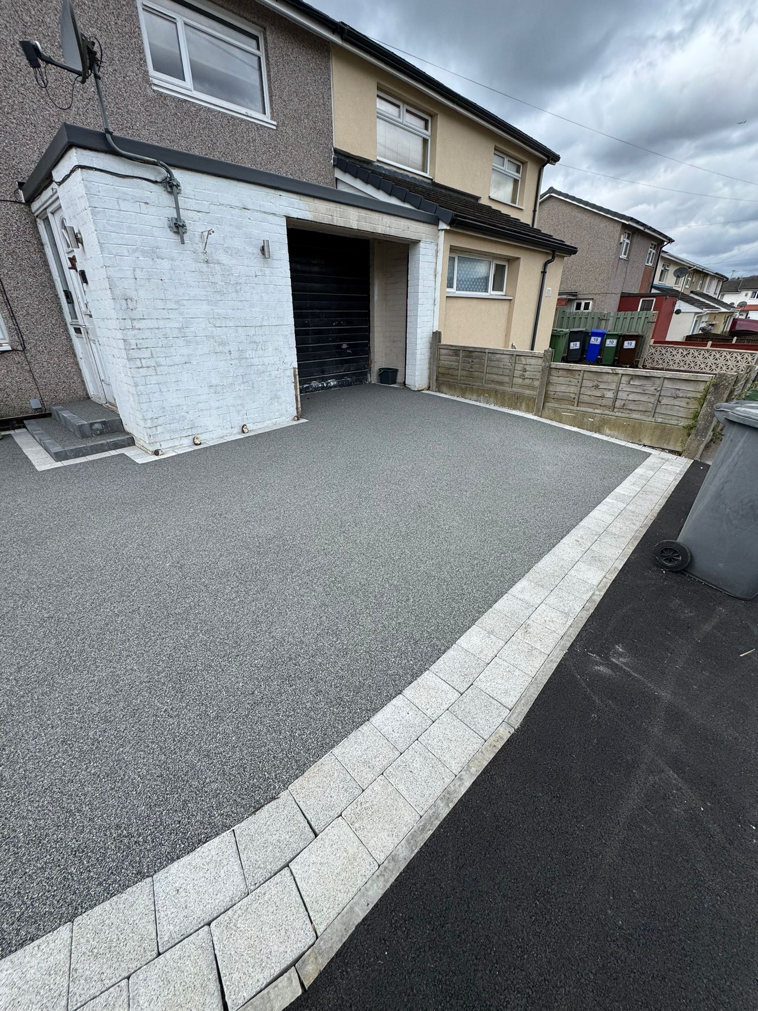Grey resin driveway with light block border leading to a black garage
