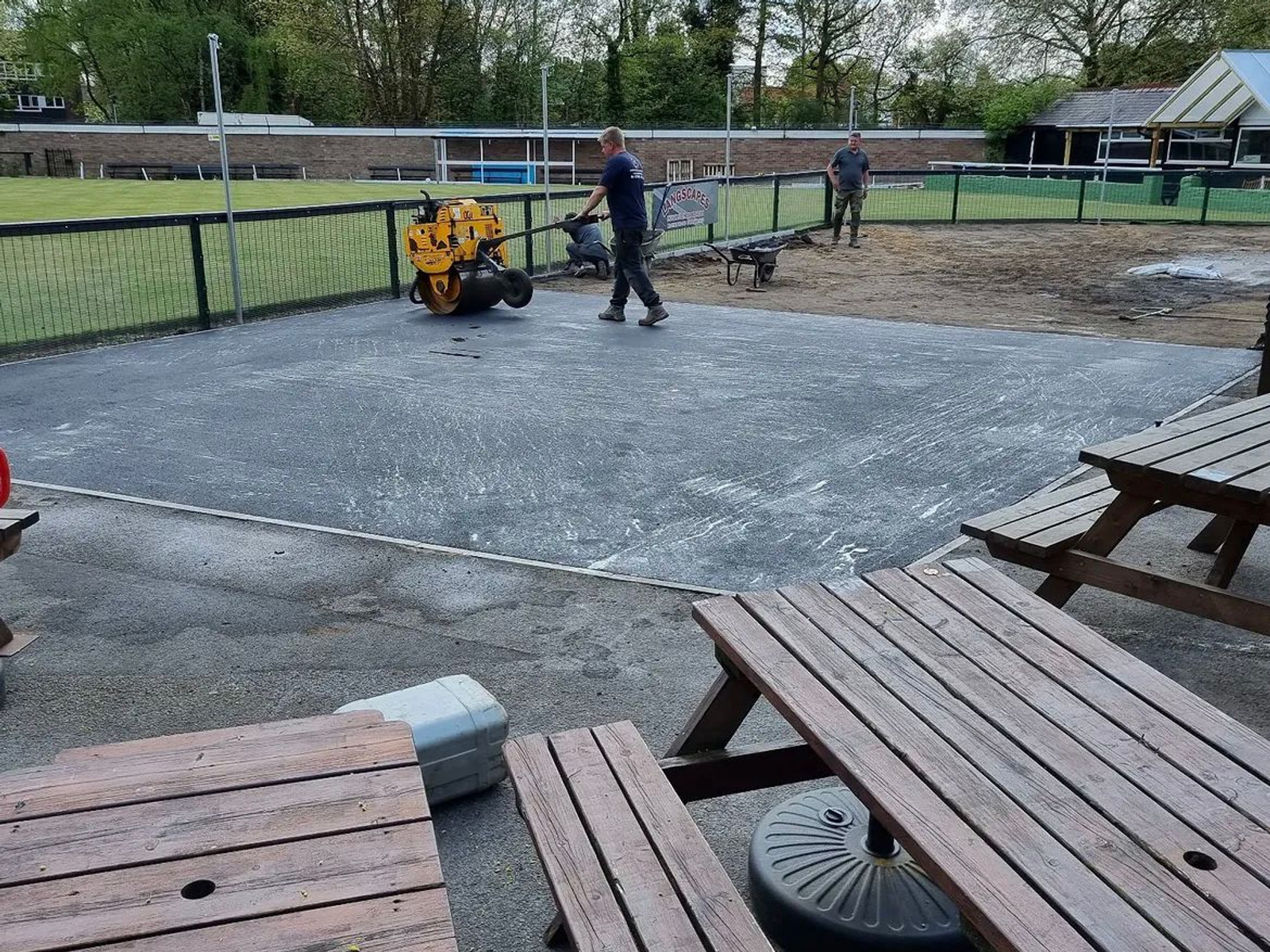 Workers compacting fresh tarmac with roller beside picnic benches / sports field — Sale & Greater Manchester