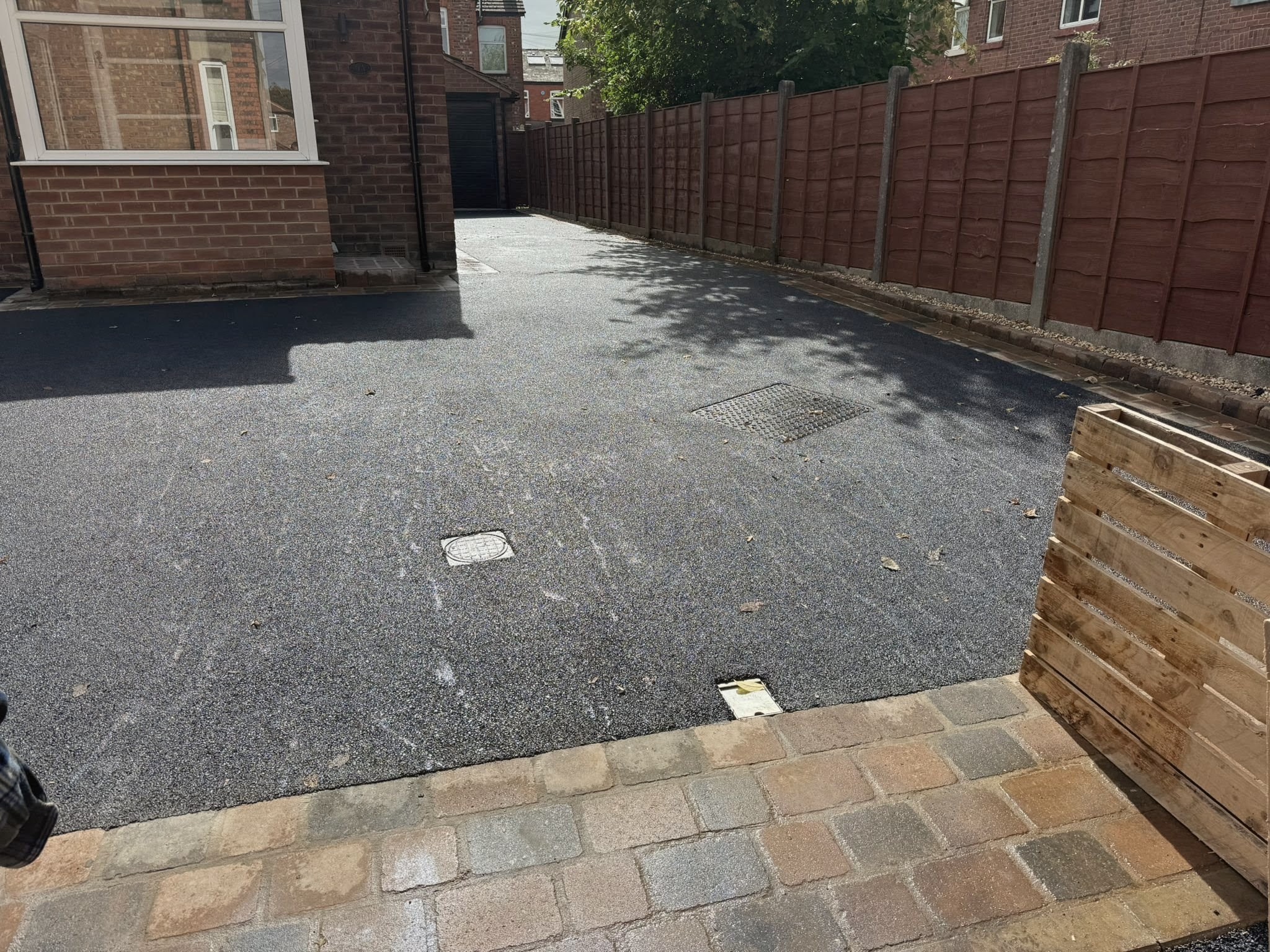 Long dark driveway with multi-tone block paving border beside a red brick house