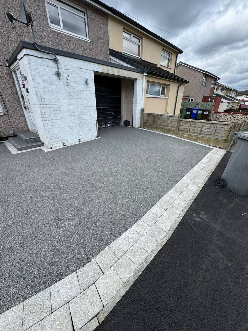 Grey resin driveway with light block border leading to a black garage